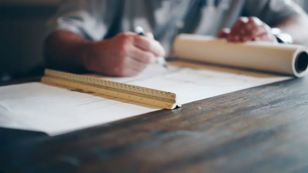 Hands drafting on a plan with a pencil and scale
